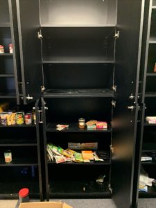 Image of black cupboards. The cupboard's doors are open and show that the shelves are mostly empty, with only a few canned items waiting to be cleared out.